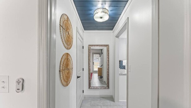 A hallway with white walls, a blue ceiling, and a tiled floor. There are two woven wall decorations and a door with a keyhole. - TN Legends Retreat 3Bd/2Ba (Murfreesboro)