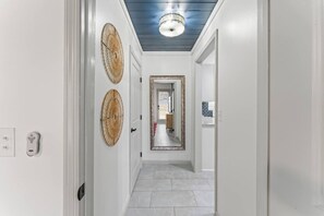 A hallway with white walls, a blue ceiling, and a tiled floor. There are two woven wall decorations and a door with a keyhole.