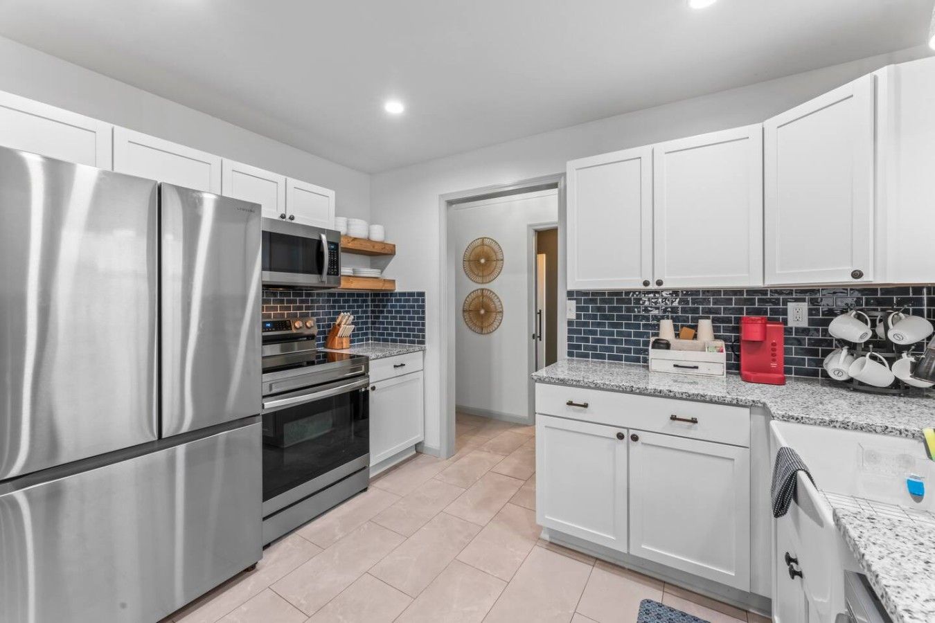 A modern kitchen with stainless steel appliances, white cabinetry, and a blue-tiled backsplash.
