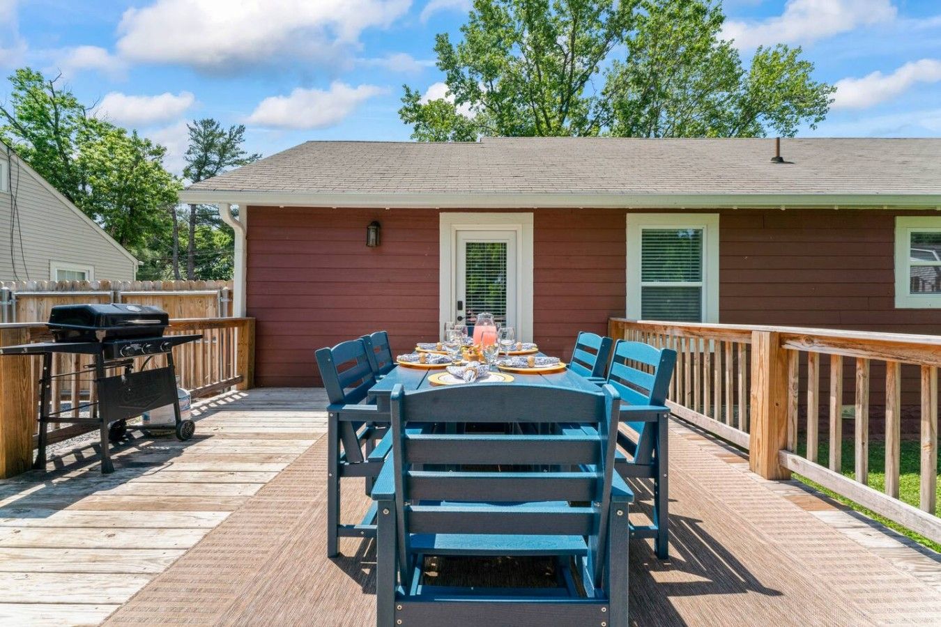 A deck with a table set for dining, a grill, and a house with a red exterior.