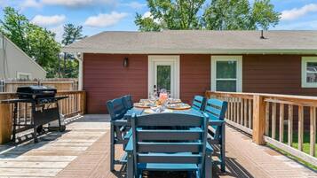 A deck with a table set for dining, a grill, and a house with a red exterior.