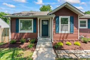 A two-story house with a front porch, a mailbox, and a small garden with shrubs and flowers.