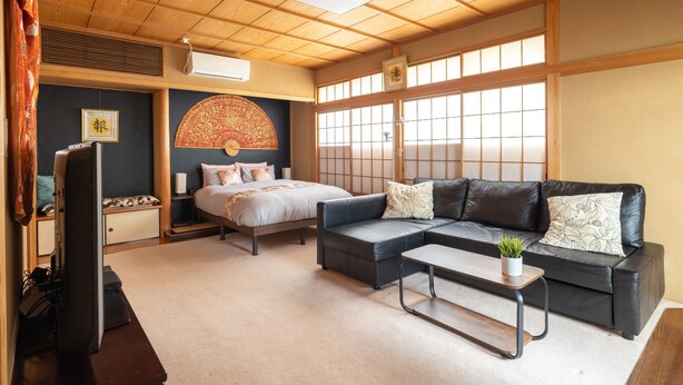 Una stanza tradizionale in stile giapponese, con pavimento in tatami, un letto basso, un divano e una TV.
