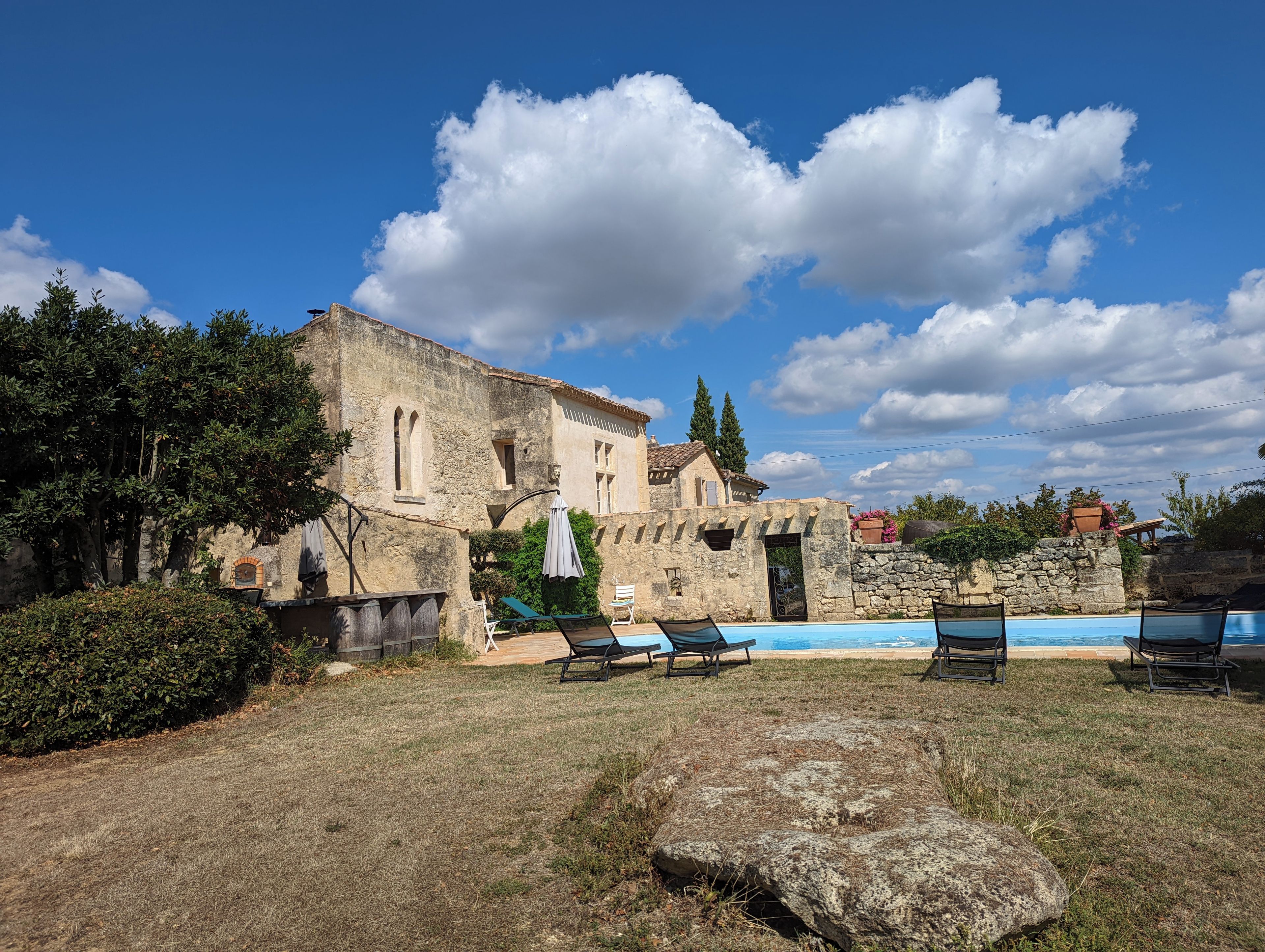 Edifício de pedra com área de piscina, espaço para sentar ao ar livre e céu limpo.
