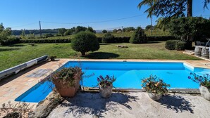 A rectangular swimming pool with a clear blue surface, surrounded by a paved deck. There are three potted plants with flowers in the foreground. - Bello Viso, Proche Saint Emilion Dans un Écrin de Verdure au Milieu des Vignes (Belvès-de-Castillon)