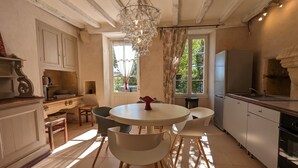 A kitchen with a round dining table, chairs, a chandelier, and a view of greenery outside. - Bello Viso, Proche Saint Emilion Dans un Écrin de Verdure au Milieu des Vignes (Belvès-de-Castillon)