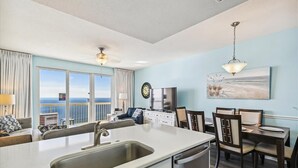 Une cuisine moderne dotée d’un grand îlot central, d’un coin repas avec des chaises, d’un téléviseur et d’un tableau accroché au mur.
