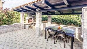An outdoor patio with a table and chairs, a stone fireplace, and a pergola overhead. - Gemütliches Pool House Tomas, in der Nähe von Pula, mit 2 Schlafzimmern (Marčana)