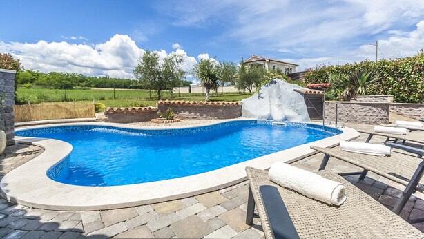 A swimming pool with a waterfall feature, surrounded by lounge chairs and a stone wall. - Gemütliches Pool House Tomas, in der Nähe von Pula, mit 2 Schlafzimmern (Marčana)
