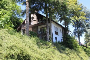 A two-story house with a balcony, surrounded by dense greenery and trees.