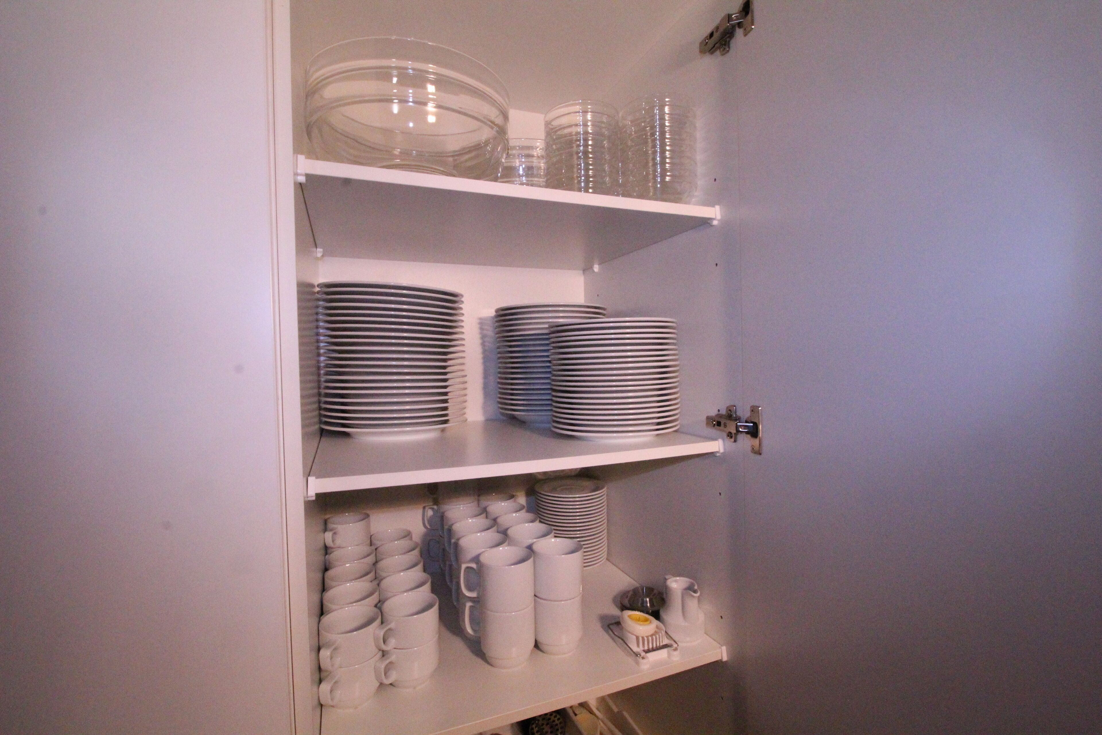 A white cabinet with shelves containing stacked plates, bowls, and mugs.