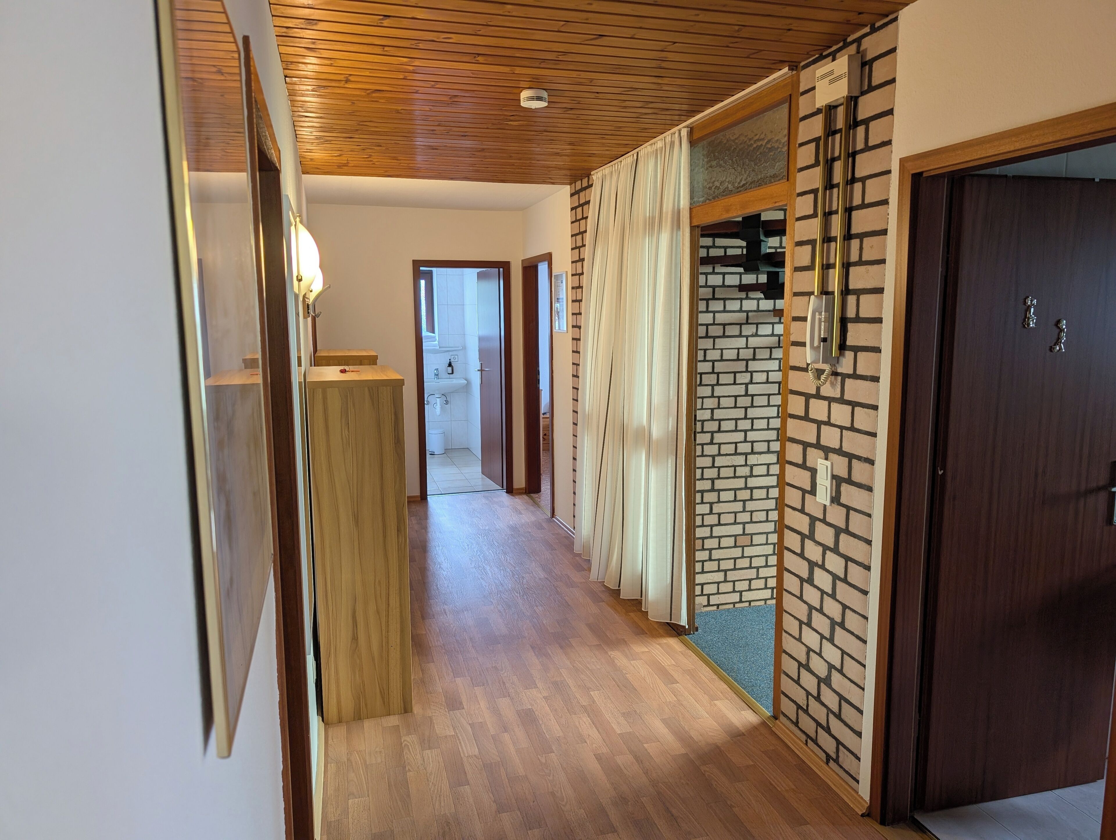 Um corredor com piso de madeira, parede de tijolos e porta de madeira.