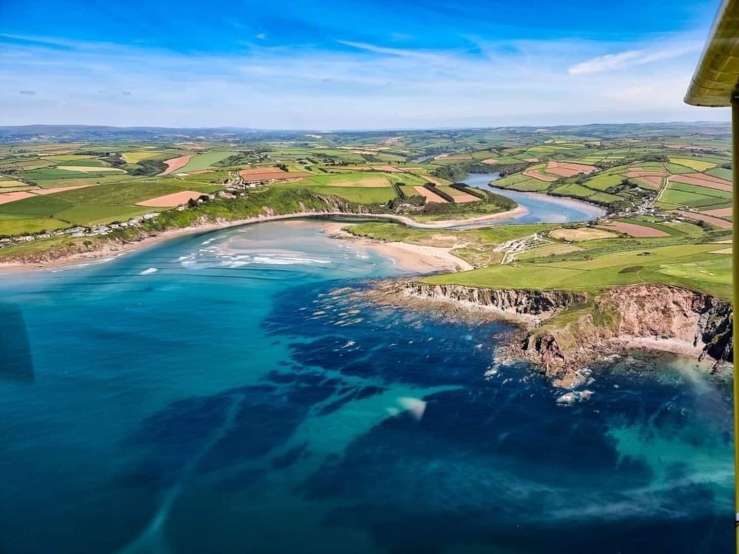 Oversigtsbillede af et kystlandskab med en snoende flod, grønne marker og en bro.