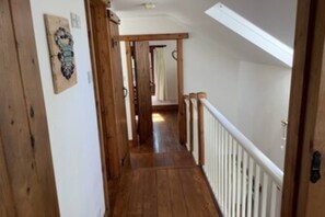 A wooden hallway with a white railing, a door on the left, and a staircase at the end.