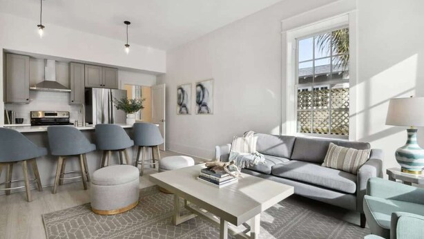 A modern living space with a kitchen, grey upholstered chairs, a grey sofa, and a patterned rug. - Bay St Louis Retreat | Downtown BSL (Bay St. Louis)