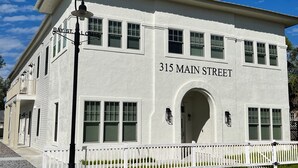 A white two-story building with the address "315 Main Street" and a white picket fence in front. - Bay St Louis Retreat | Downtown BSL (Bay St. Louis)