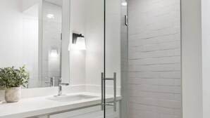 A modern bathroom with a glass-enclosed shower, white cabinetry, and a large mirror. - Bay St Louis Retreat | Downtown BSL (Bay St. Louis)