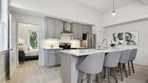 A modern kitchen with grey cabinets, stainless steel appliances, and a central island with bar stools. - Bay St Louis Retreat | Downtown BSL (Bay St. Louis)