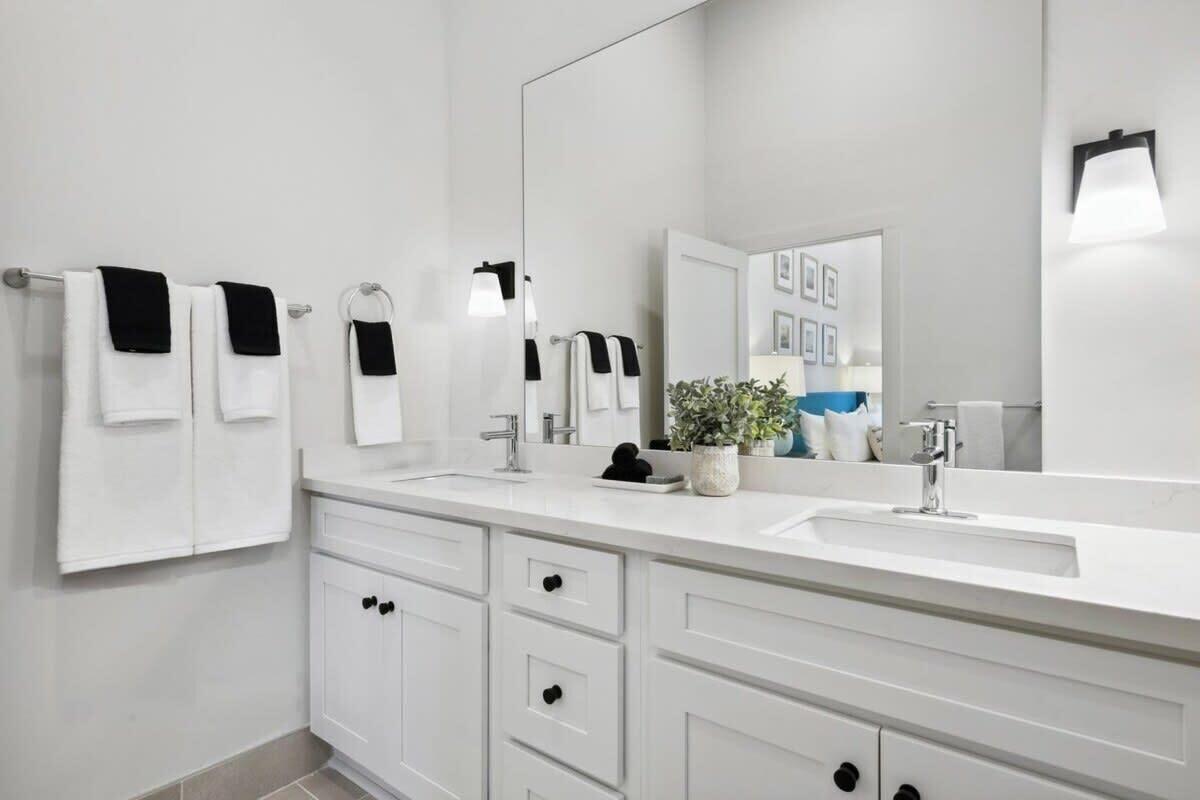 A modern bathroom with two sinks, a large mirror, and white cabinetry.