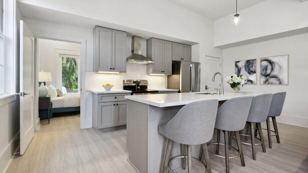 A modern kitchen with grey cabinets, a stainless steel refrigerator, and a central island with bar stools.