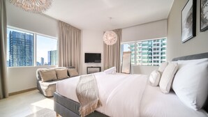 A modern bedroom with a large bed, a flat-screen TV, and a view of the cityscape through large windows. - Colossal 2BR at MAG 218 Dubai Marina by Deluxe Holiday Homes (Dubai)