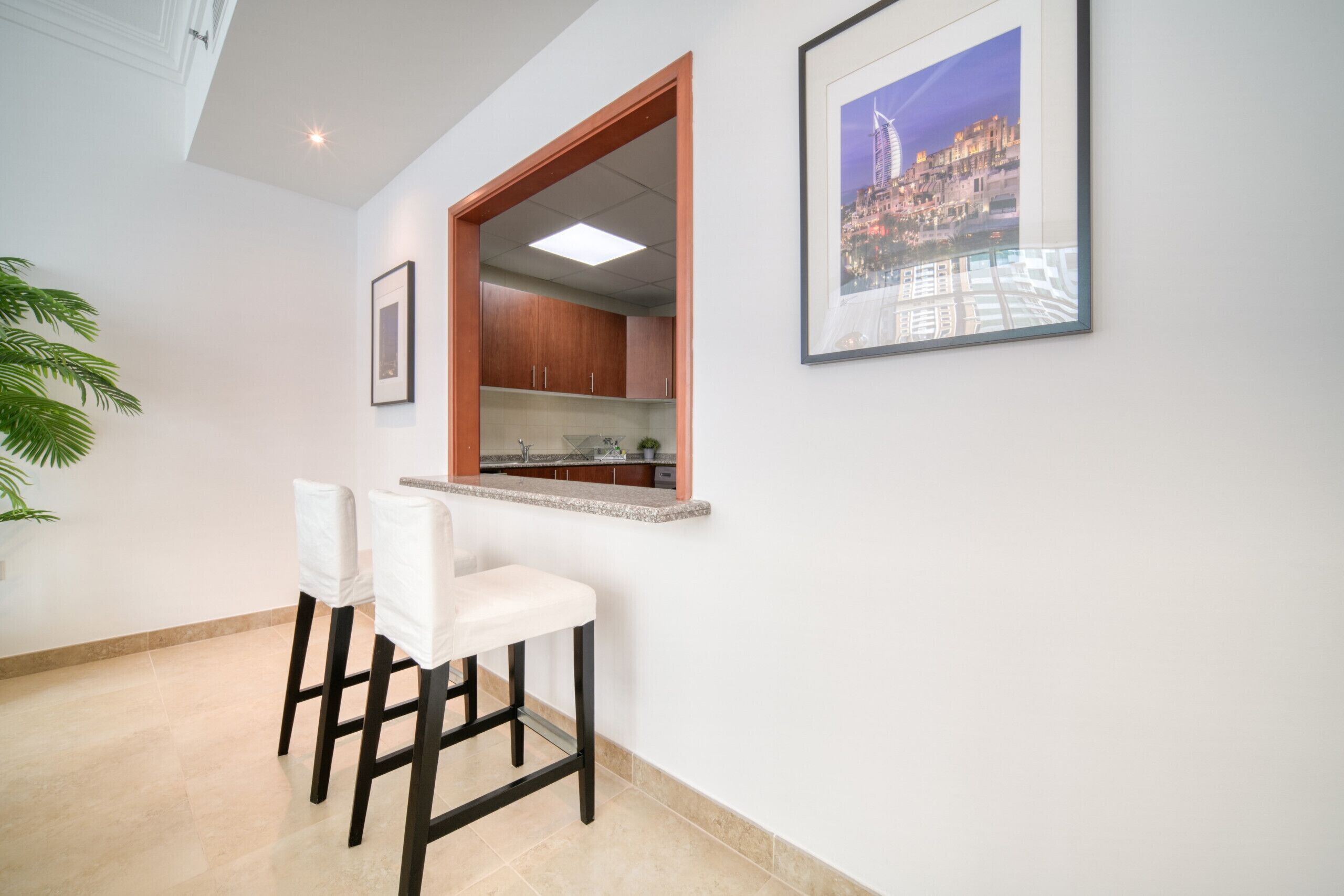 Una cocina moderna con ventana, un área de comedor con dos sillas y un cuadro con una vista urbana en la pared.