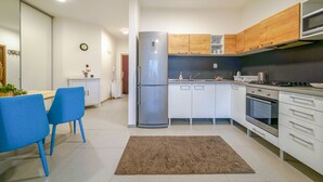 Een moderne keuken met witte kasten, een roestvrijstalen koelkast, een magnetron en een fornuis. Er is een eethoek met blauwe stoelen en een kleine tafel.