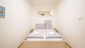 Een kleine kamer met een bed, nachtkastje, spiegel en een aan de muur hangend schilderij.