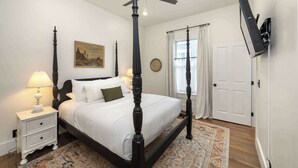 A four-poster bed with a ceiling fan, a painting on the wall, a white door, and a mounted television. - 1BR Downtown, Close to Cincinnati Stadiums & Bars (Covington)