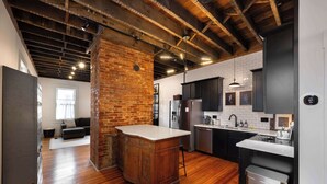 A modern kitchen with a brick wall, wooden flooring, and stainless steel appliances. - 1BR Downtown, Close to Cincinnati Stadiums & Bars (Covington)