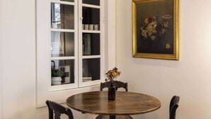 A dining area with a round wooden table, four black chairs, a white cabinet with glass doors, and a framed painting on the wall. - 1BR Downtown, Close to Cincinnati Stadiums & Bars (Covington)