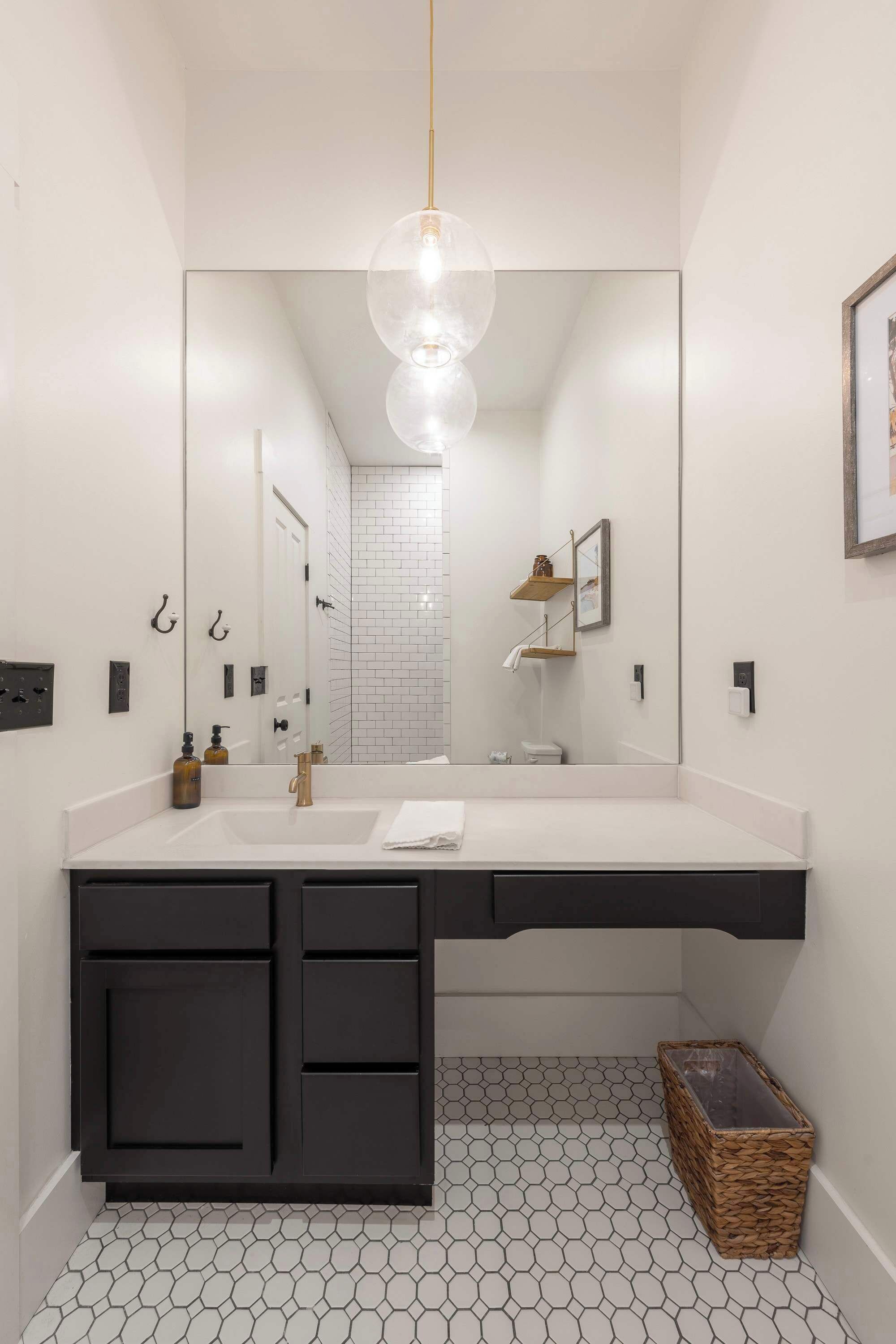 A modern bathroom with a large mirror, a white countertop, black cabinets, and a hexagonal patterned floor.