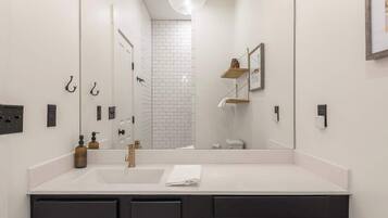 A modern bathroom with a large mirror, a white countertop, black cabinets, and a hexagonal patterned floor.