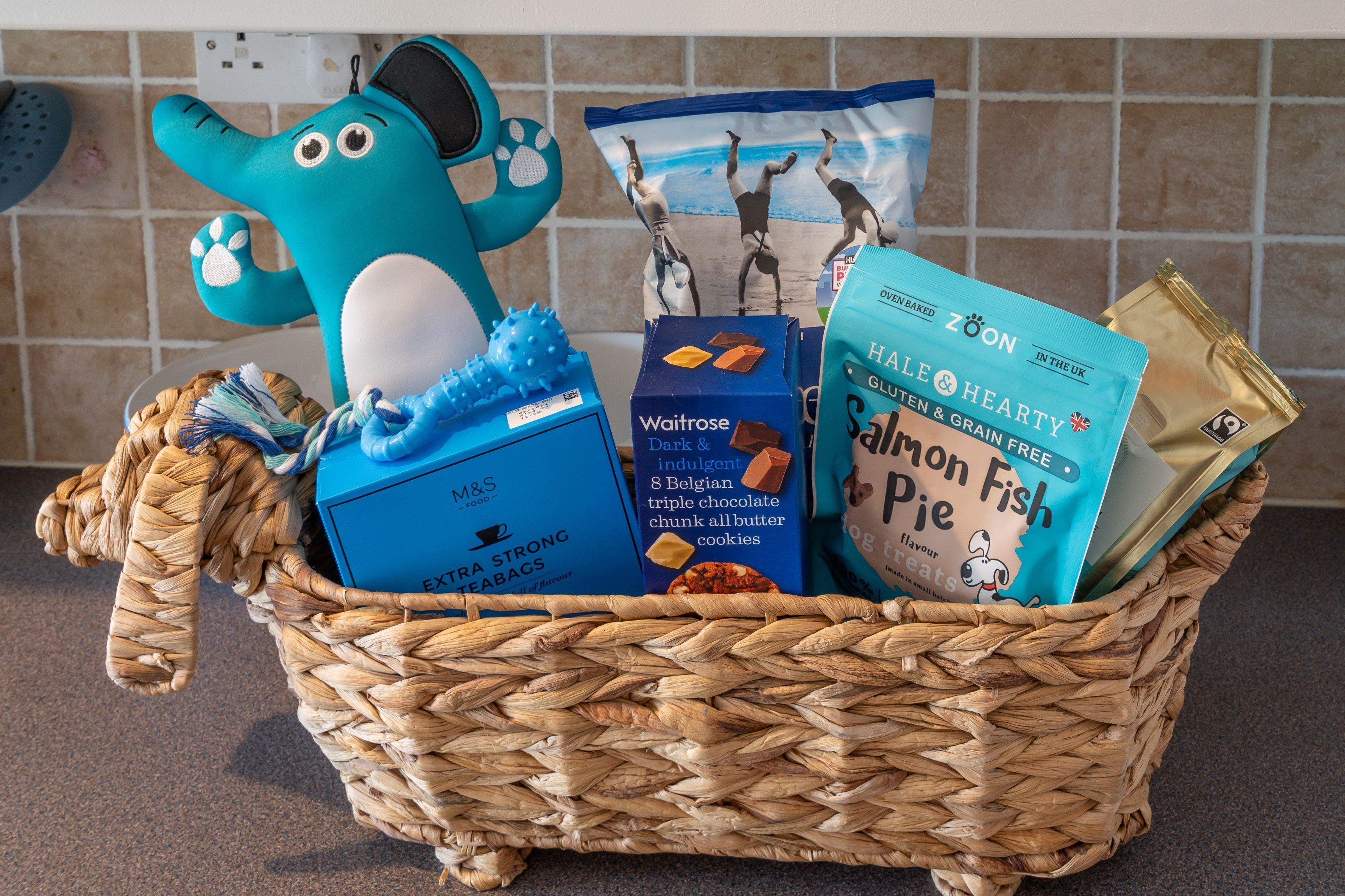 A wicker basket containing various food items and a blue plush toy.