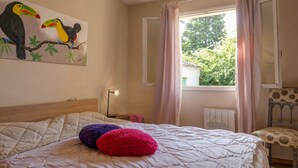 A bedroom with a bed, a painting of toucans, a window with curtains, a radiator, and a chair. - Village house in the heart of Saint-Paul-Trois-Châteaux, Drôme Provençale (Saint-Paul-Trois-Châteaux)
