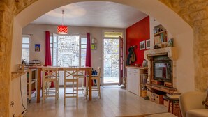 A cozy living area with a stone archway, a dining table with chairs, a fireplace, and a television. - Village house in the heart of Saint-Paul-Trois-Châteaux, Drôme Provençale (Saint-Paul-Trois-Châteaux)