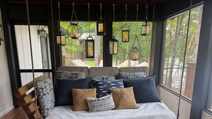 A wooden swing bed with patterned cushions and a pillow with text, hanging from a rope, in a room with large windows and hanging lanterns. - Hickory Hideaway on Tim`s Ford Lake, Boat rental available (Winchester)