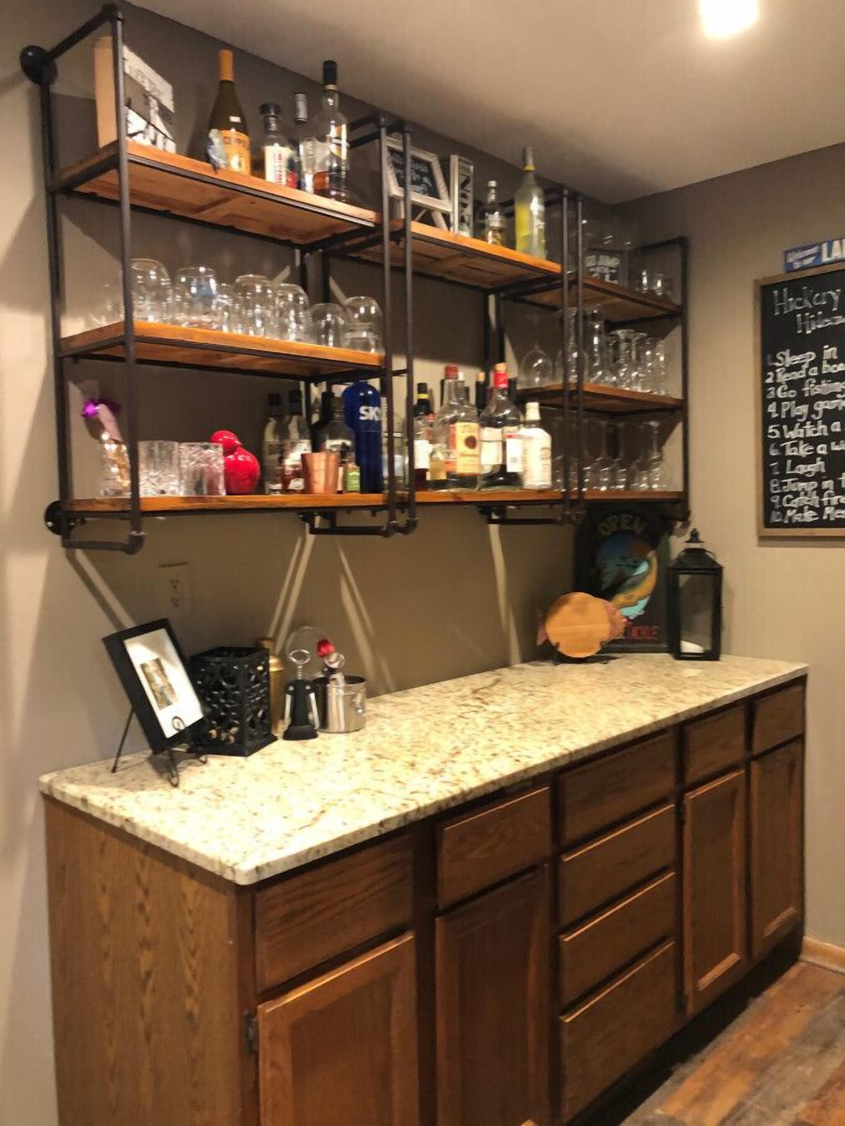 A bar area with wooden shelves holding bottles and glasses, a marble countertop, and a chalkboard menu.