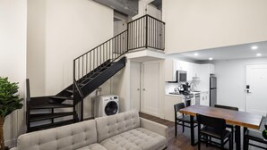 A compact living space with a sofa, dining table, chairs, a staircase, and a kitchen area. - Sosuite | 2BR Loft w Shared W/D, Gym, Lounge (Philadelphia)