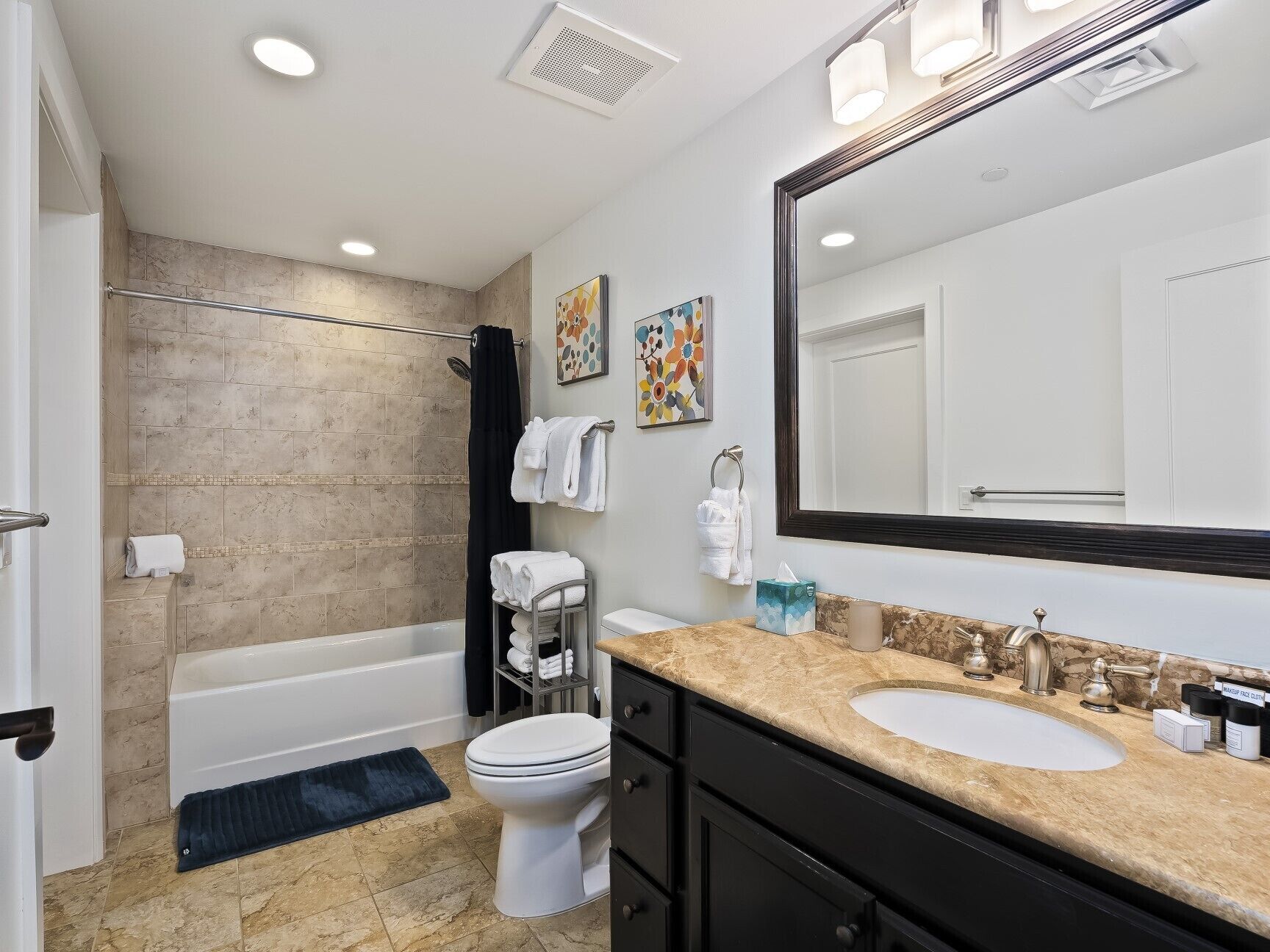 A modern bathroom with a bathtub, toilet, and sink. There are towels and toiletries on the counter.