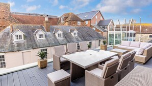 A rooftop patio with wicker furniture, a glass table, and a view of traditional brick buildings. - Vitamin Sea - Sun Terrace Overlooking Poole Quay (Poole)