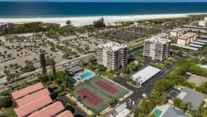 An aerial view of a coastal area with a beach, parking lots, and multi-story buildings.