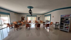 Un grand espace dédié à la salle à manger, avec plusieurs tables et chaises, un ventilateur de plafond et un réfrigérateur rempli de boissons.