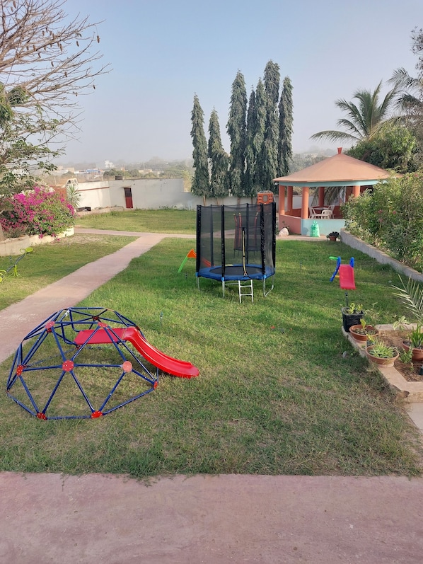 A grassy outdoor area with a trampoline, a red slide, and a geodesic dome structure.