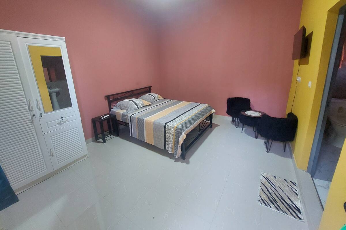 A bedroom with a bed, a wardrobe, a small table, and a chair.