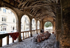 An arched corridor with stone flooring and wooden beams, lined with baskets and a red and black striped cloth. - Inglenook Cottage - Broad Campden, Chipping Campden, sleeps 2 guests  in 1 bedroom (Broad Campden)