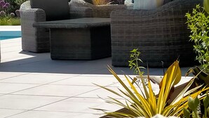 Uma área de pátio com piscina, móveis de exterior e plantas em vasos.