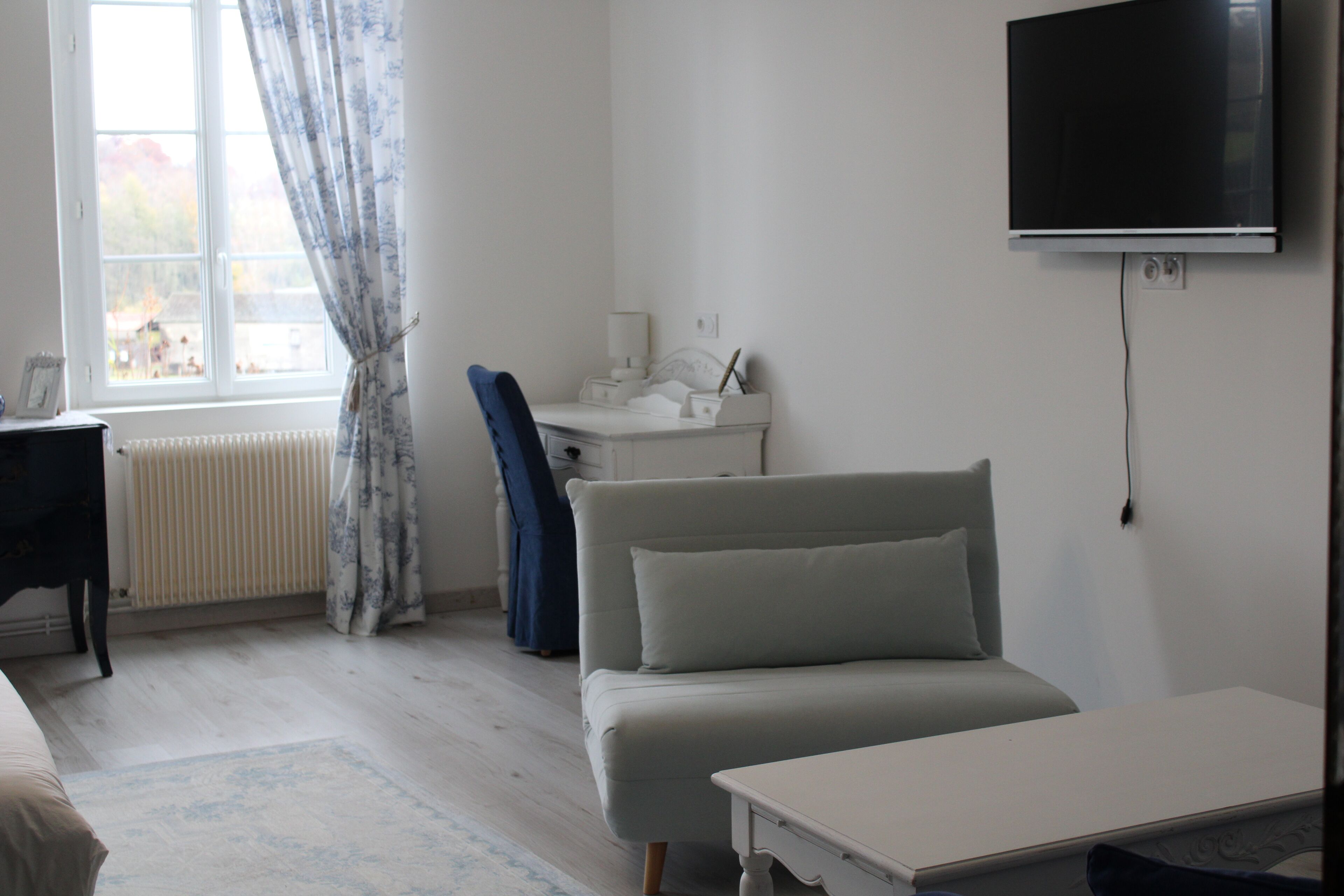 A room with a bed, a desk, a chair, a TV, and a window with curtains.