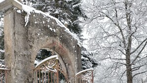 Um jardim coberto de neve com um arco de pedra e um portão de metal.