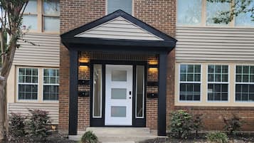 A two-story building with a brick facade, a central entrance with a black trim, and a small porch area with lighting.